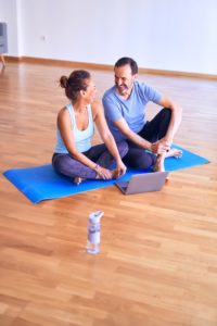 yoga benefits, yoga for moms, yoga, yoga for couples, yoga relationship benefits, Middle age beautiful sporty couple smiling happy. Sitting on mat with smile on face using laptop at gym